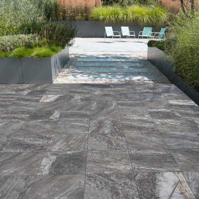 Pátio com pavimento e revestimento cerâmico que imita pedra quartzito, com realismo e veios marcados, série Pukka Anthracite da Recer.